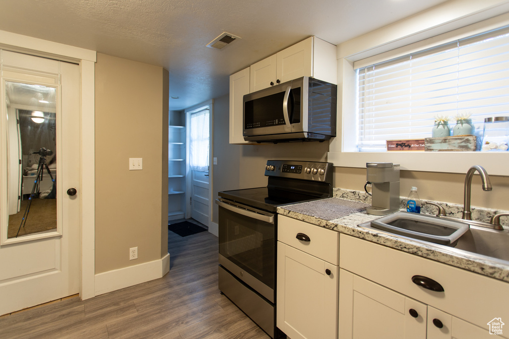 Kitchen featuring visible vents, wood finished floors, a sink, baseboards, and stainless steel appliances