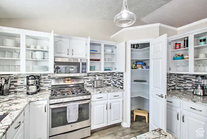 Kitchen featuring white cabinets, stainless steel appliances, decorative backsplash, open shelves, and light stone countertops