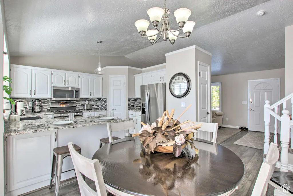 Dining area with lofted ceiling, an inviting chandelier, wood finished floors, and a textured ceiling