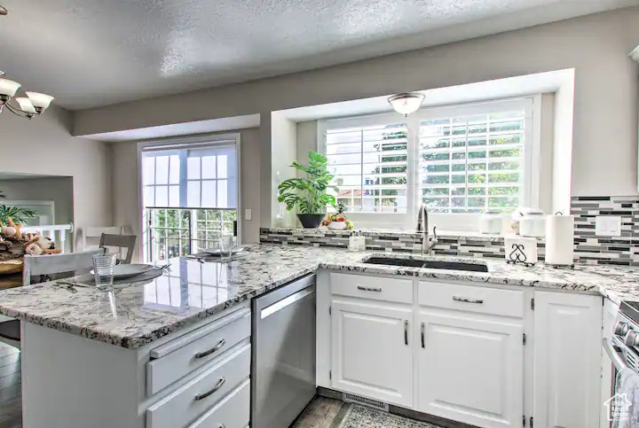 Kitchen with white cabinets, a peninsula, a sink, light stone counters, and appliances with stainless steel finishes