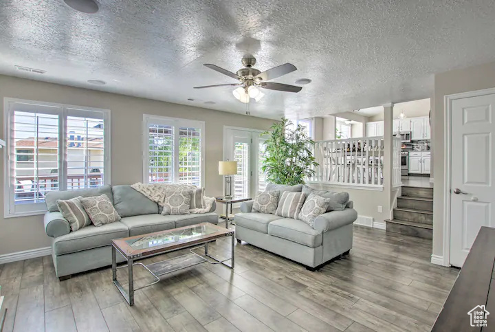 Living area featuring wood finished floors, a textured ceiling, stairs, ceiling fan, and baseboards