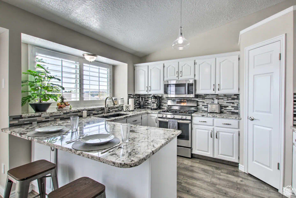 Kitchen with a sink, a peninsula, appliances with stainless steel finishes, a breakfast bar area, and white cabinetry