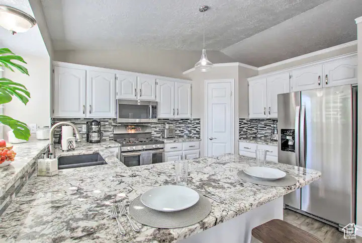 Kitchen with white cabinets, lofted ceiling, light stone counters, a sink, and appliances with stainless steel finishes