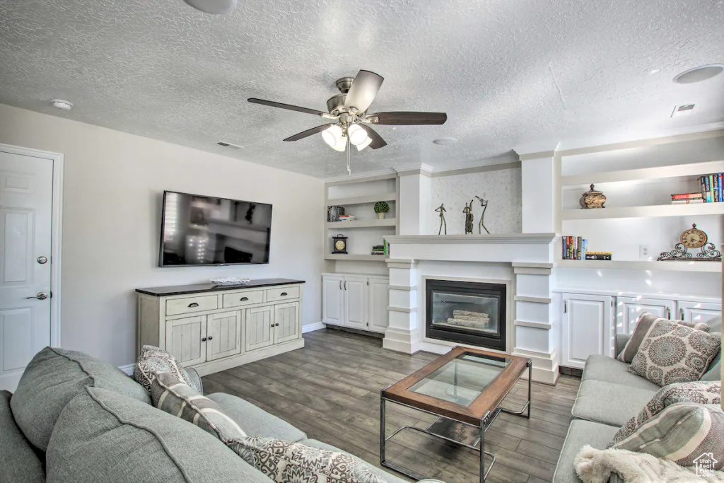 Living room featuring a glass covered fireplace, a textured ceiling, dark wood-style floors, and ceiling fan