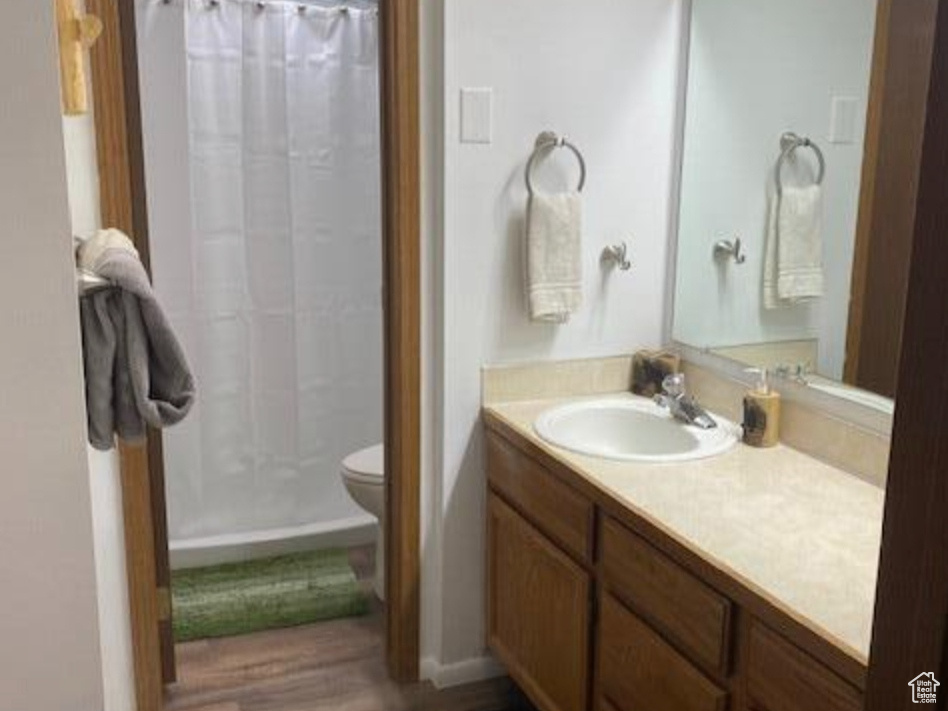Full bath featuring a shower with curtain, toilet, baseboards, wood finished floors, and vanity