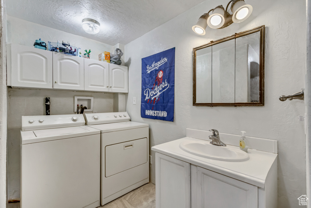 Laundry area with washer and dryer, a textured wall, laundry area, a sink, and a textured ceiling