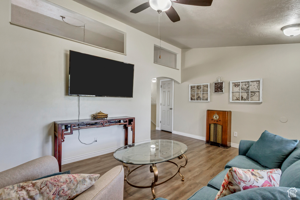 Living room with arched walkways, ceiling fan, vaulted ceiling, and wood finished floors