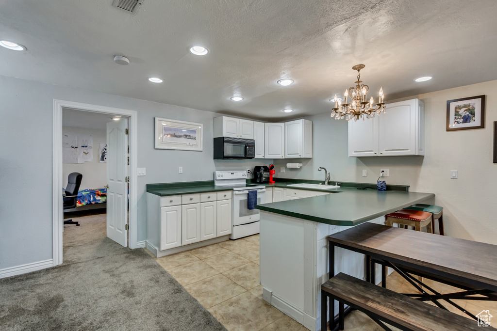 Kitchen featuring white electric stove, black microwave, a sink, a peninsula, and white cabinetry