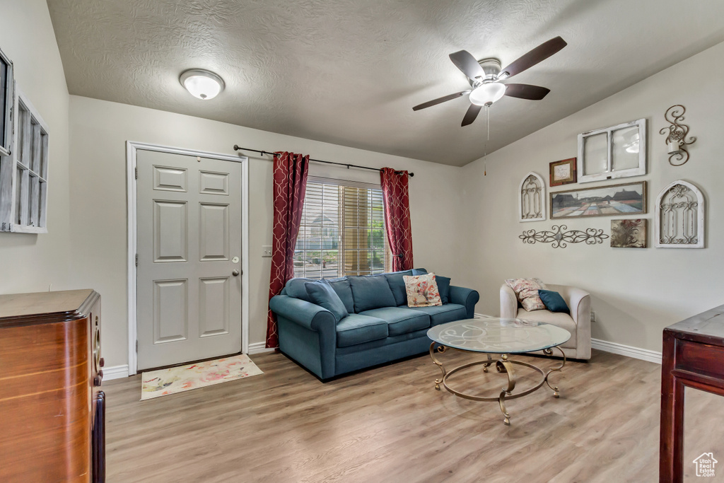 Living room featuring a ceiling fan, baseboards, wood finished floors, and a textured ceiling