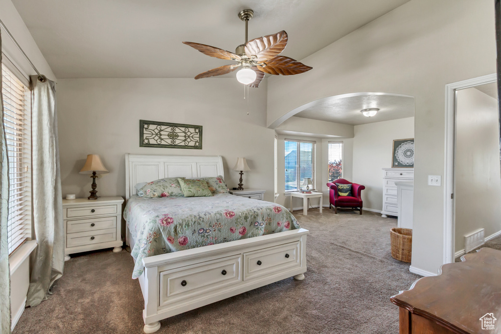 Carpeted bedroom with arched walkways, ceiling fan, and high vaulted ceiling