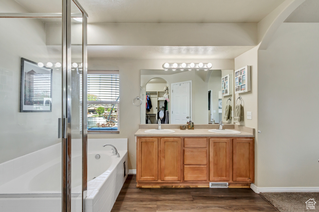 Full bath featuring double vanity, a sink, a garden tub, and wood finished floors