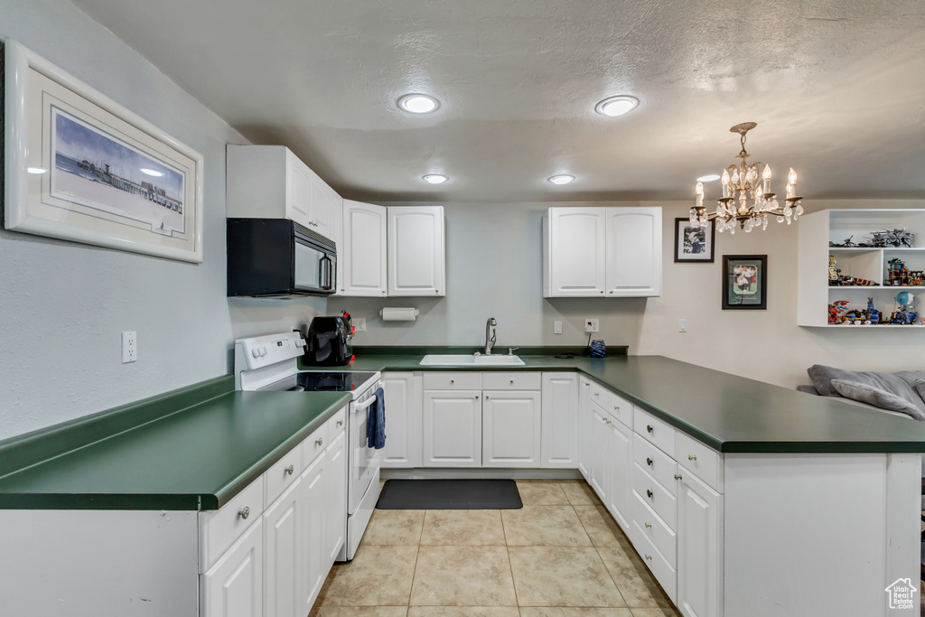 Kitchen with a peninsula, black microwave, dark countertops, white range with electric cooktop, and a sink
