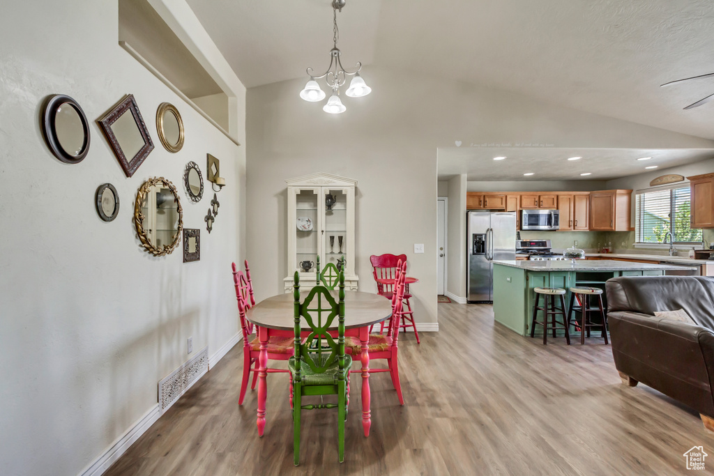 Dining area featuring an inviting chandelier, baseboards, light wood finished floors, and lofted ceiling
