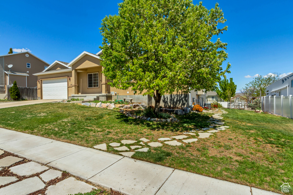 View of front of property with fence, a garage, stucco siding, a front yard, and concrete driveway