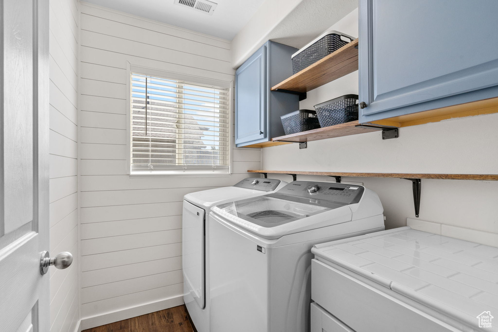 Washroom featuring washer and dryer, dark wood-style flooring, wooden walls, and cabinet space