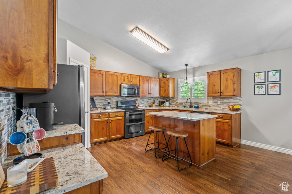 Kitchen featuring appliances with stainless steel finishes, decorative backsplash, brown cabinets, and lofted ceiling