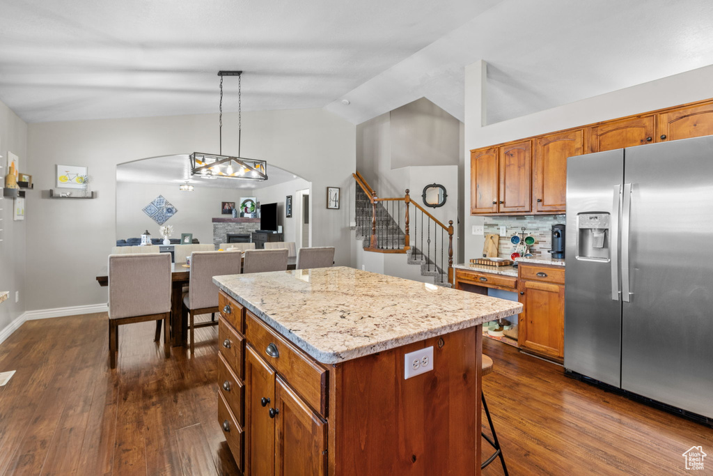 Kitchen featuring dark wood-style flooring, stainless steel fridge, arched walkways, a center island, and lofted ceiling