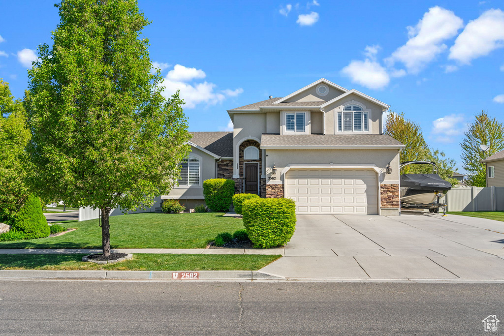 Traditional-style home featuring a garage, driveway, a front lawn, and stucco siding