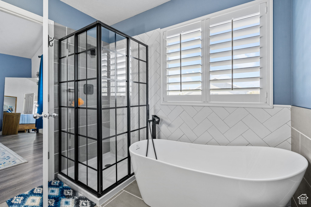 Bathroom featuring wainscoting, french doors, tile walls, a soaking tub, and a stall shower