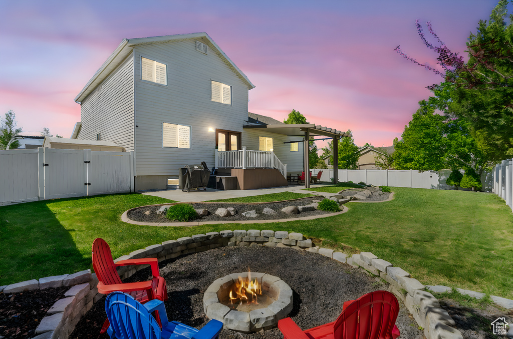 Back of property at dusk featuring an outdoor fire pit, a fenced backyard, a gate, a patio area, and a yard