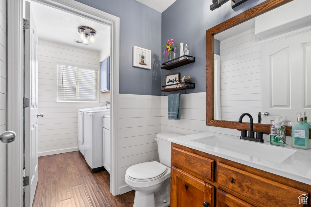 Bathroom with wood finished floors, vanity, toilet, wooden walls, and washer and clothes dryer