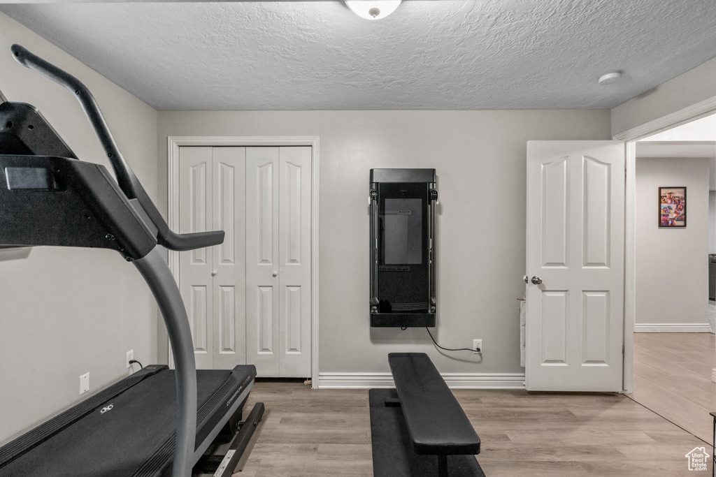 Exercise area with light wood-style floors, baseboards, and a textured ceiling