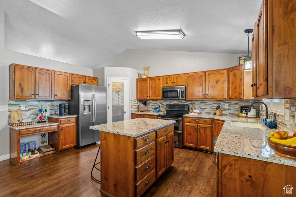 Kitchen featuring appliances with stainless steel finishes, brown cabinetry, a center island, lofted ceiling, and backsplash