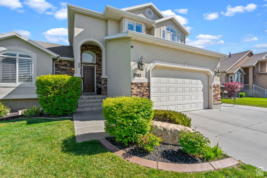 View of front of property featuring a front yard, stone siding, stucco siding, an attached garage, and driveway