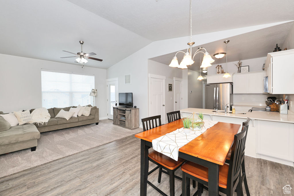 Dining room featuring visible vents, ceiling fan with notable chandelier, light wood finished floors, and lofted ceiling