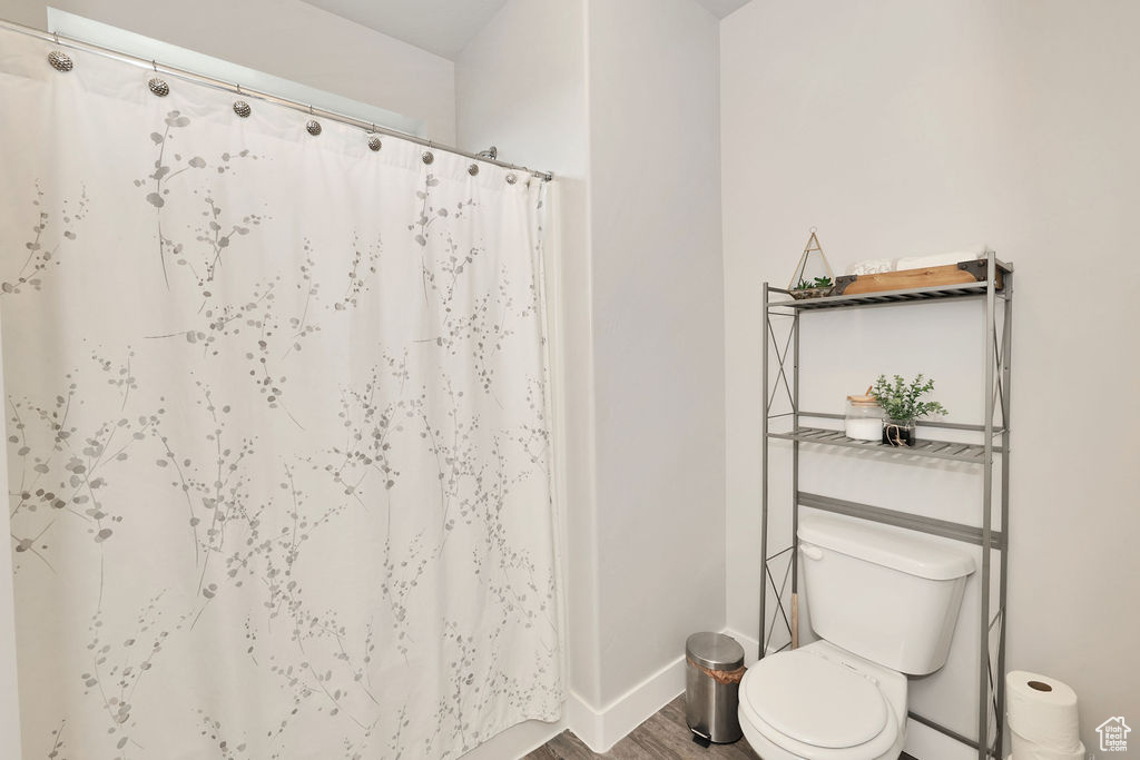 Full bath featuring baseboards, a shower with shower curtain, wood finished floors, and toilet