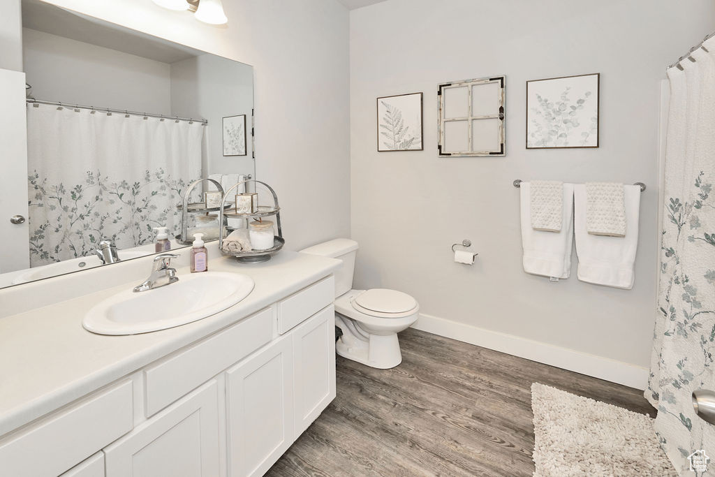 Full bathroom with vanity, baseboards, toilet, and wood finished floors