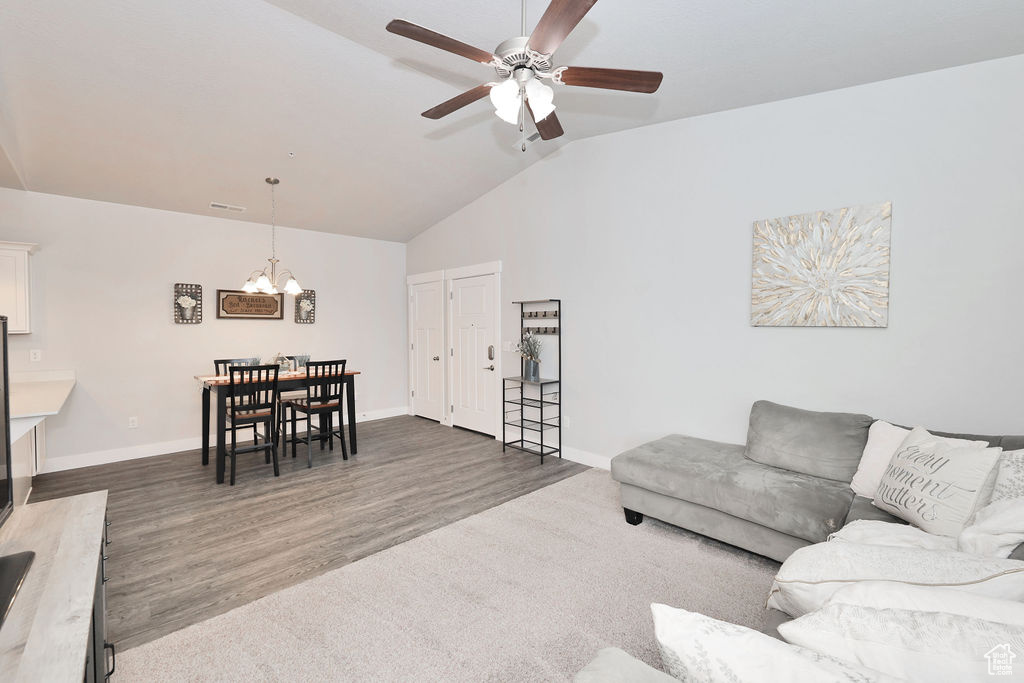 Living room featuring dark wood-style flooring, baseboards, vaulted ceiling, and ceiling fan with notable chandelier
