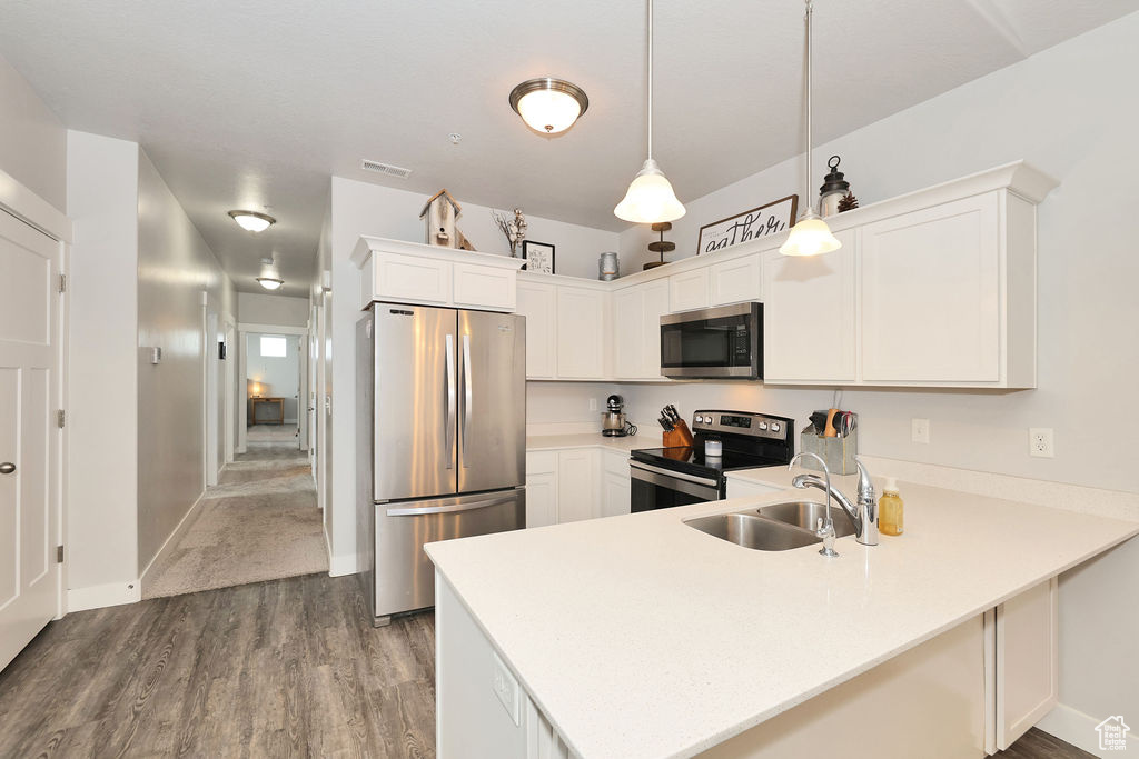Kitchen with visible vents, a peninsula, wood finished floors, a sink, and appliances with stainless steel finishes