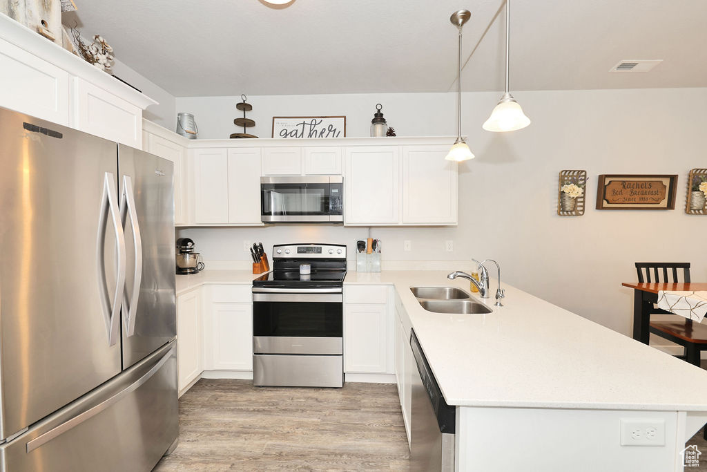 Kitchen featuring appliances with stainless steel finishes, a sink, light wood finished floors, light countertops, and a peninsula