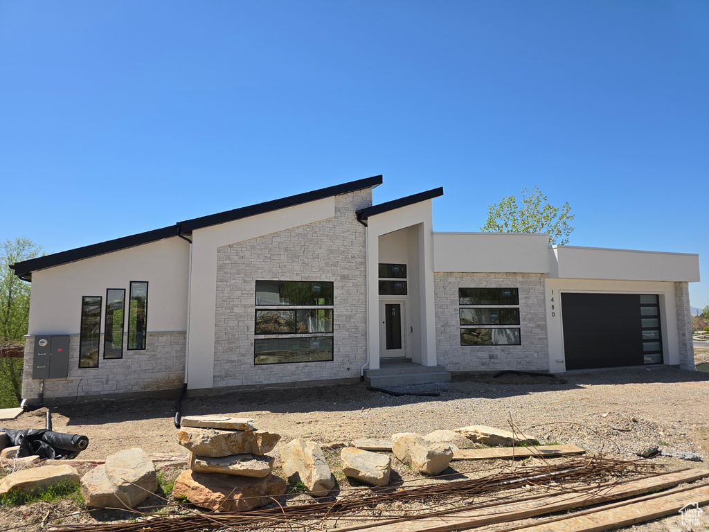 Contemporary home with a garage, dirt driveway, stucco siding, and stone siding