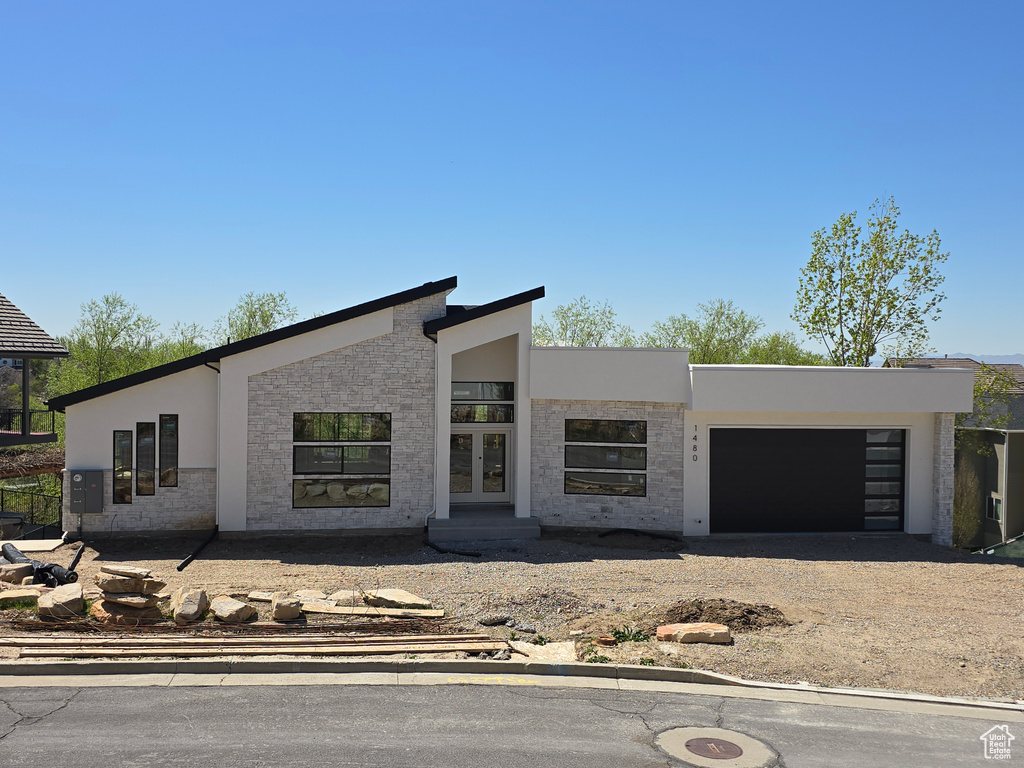 Contemporary home featuring a garage, stone siding, stucco siding, french doors, and driveway