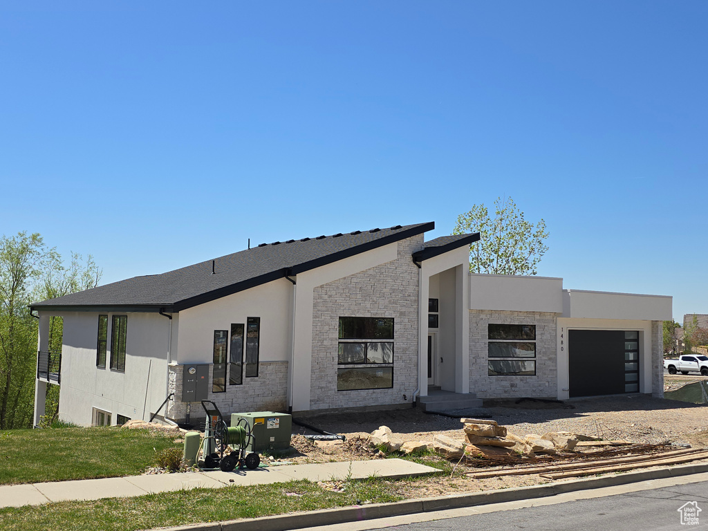 View of front of property featuring an attached garage, stucco siding, driveway, and stone siding