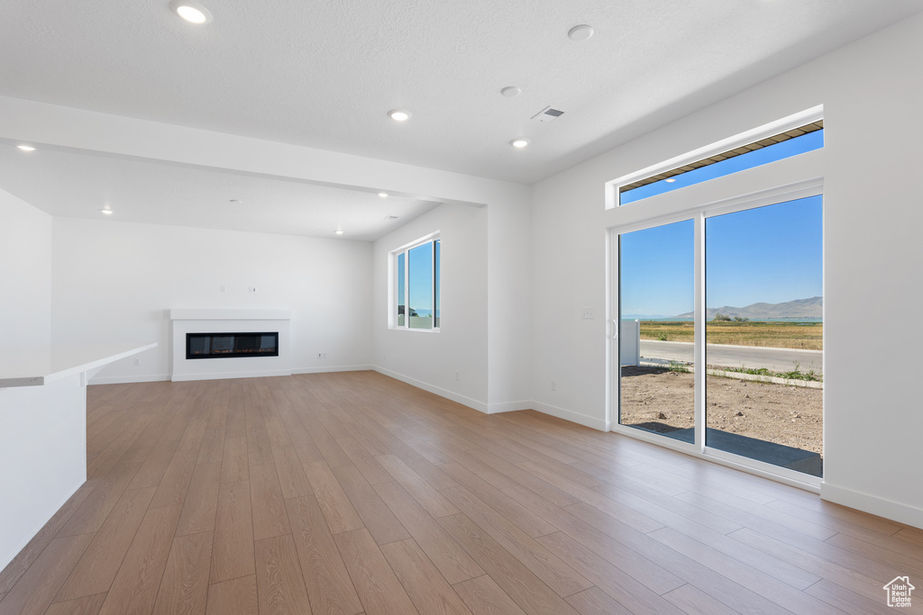 Unfurnished living room with light wood finished floors, a mountain view, baseboards, and a glass covered fireplace