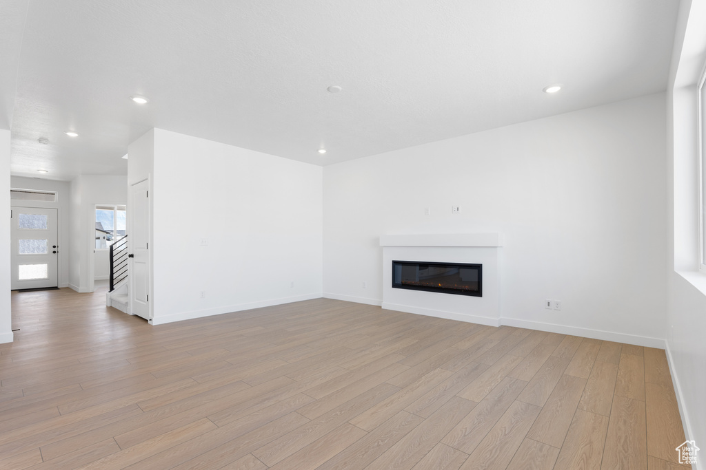 Unfurnished living room with recessed lighting, stairway, light wood finished floors, baseboards, and a glass covered fireplace