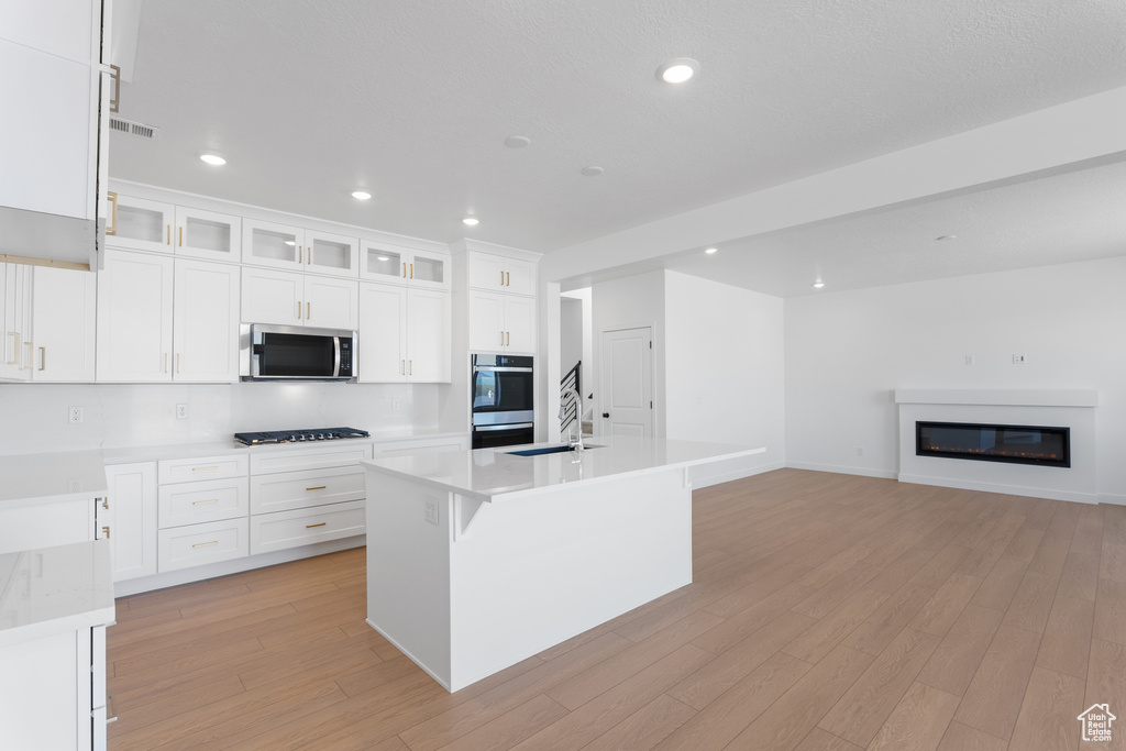 Kitchen featuring white cabinets, light wood finished floors, light countertops, and stainless steel microwave