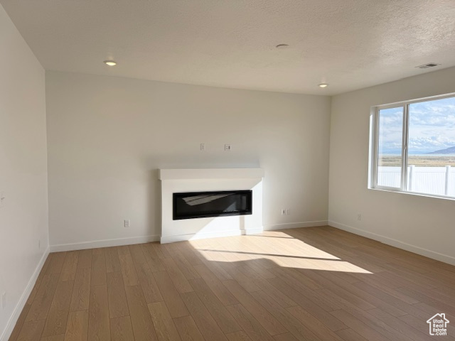 Unfurnished living room with visible vents, wood finished floors, baseboards, a glass covered fireplace, and recessed lighting