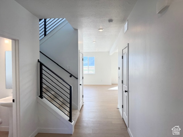 Corridor featuring a textured ceiling, visible vents, light wood-type flooring, stairway, and baseboards