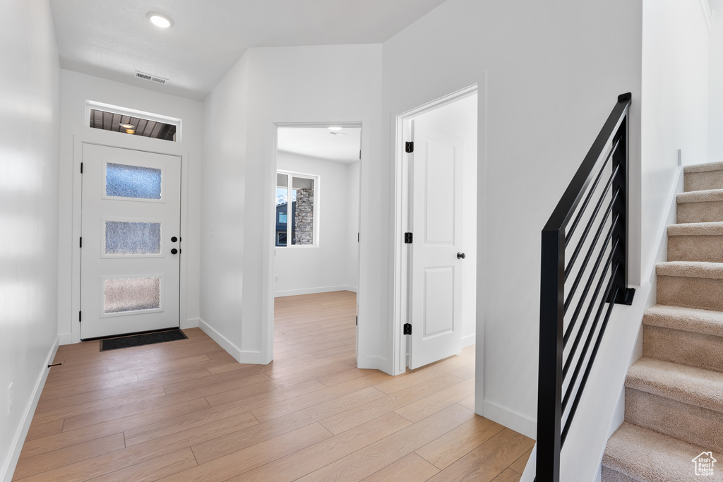 Entrance foyer with baseboards, stairs, visible vents, and light wood-type flooring