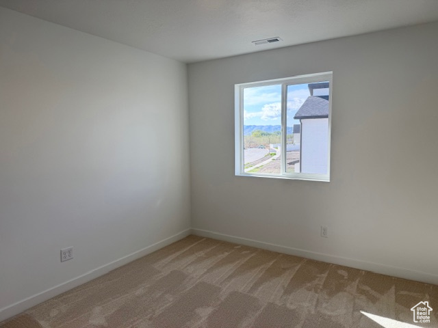 Unfurnished room featuring baseboards, visible vents, and light colored carpet