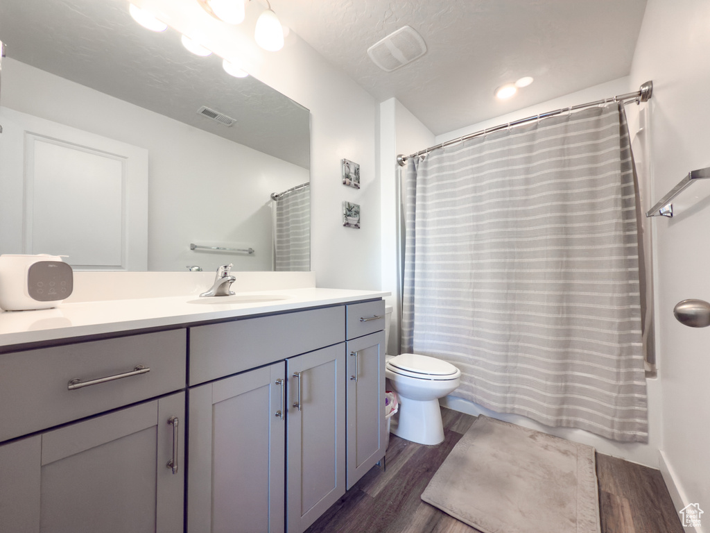 Full bath with toilet, visible vents, wood finished floors, and vanity