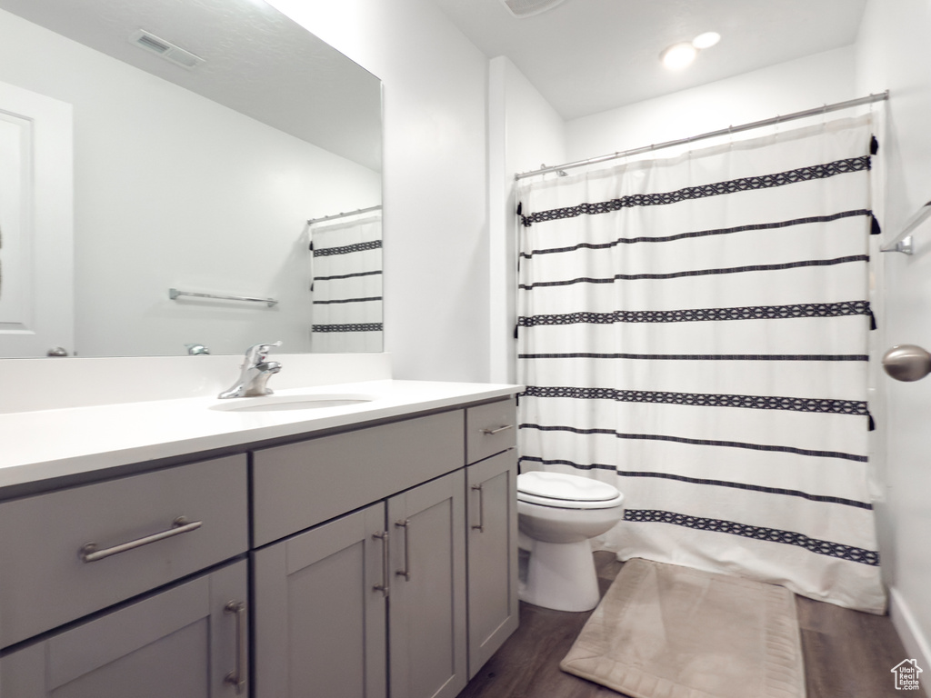 Bathroom with vanity, toilet, curtained shower, wood finished floors, and visible vents