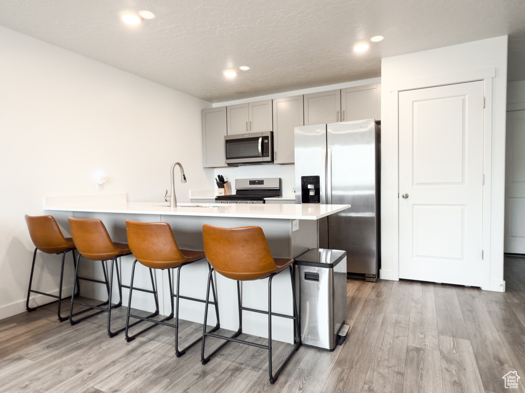 Kitchen with gray cabinets, a breakfast bar, stainless steel appliances, and light wood finished floors