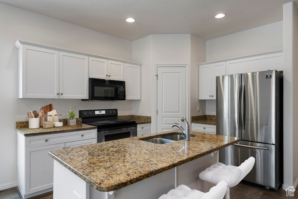 Kitchen with appliances with stainless steel finishes, a breakfast bar, white cabinets, and a sink