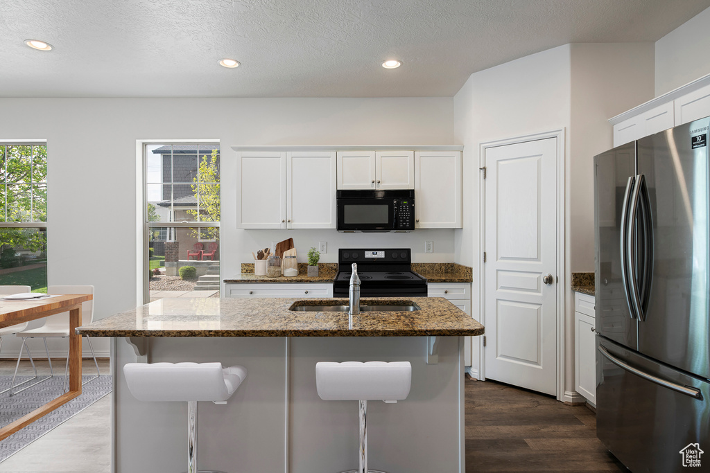 Kitchen with dark wood-style floors, black appliances, a sink, and dark stone counters
