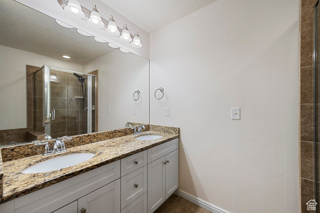 Full bathroom with tile patterned floors, a shower stall, double vanity, and a sink